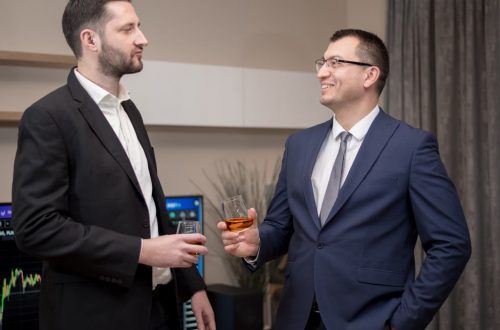 Two business professionals socializing indoors, wearing formal attire, engaging in a friendly conversation.