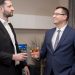 Two business professionals socializing indoors, wearing formal attire, engaging in a friendly conversation.
