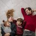 Smiling family of four lying on a blanket, sharing happiness and love indoors.