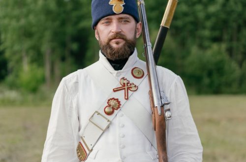 Man in historical military uniform with rifle, outdoors in summer.