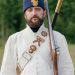 Man in historical military uniform with rifle, outdoors in summer.